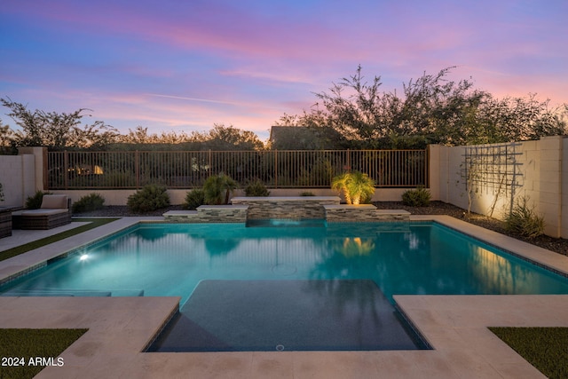 pool at dusk featuring a hot tub