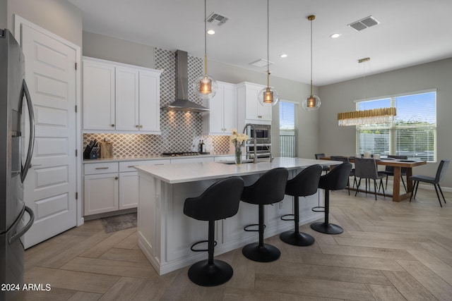 kitchen featuring decorative backsplash, light parquet flooring, hanging light fixtures, ventilation hood, and a center island with sink