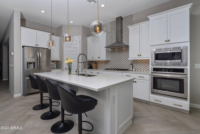 kitchen featuring appliances with stainless steel finishes, decorative backsplash, a center island with sink, wall chimney range hood, and light parquet floors