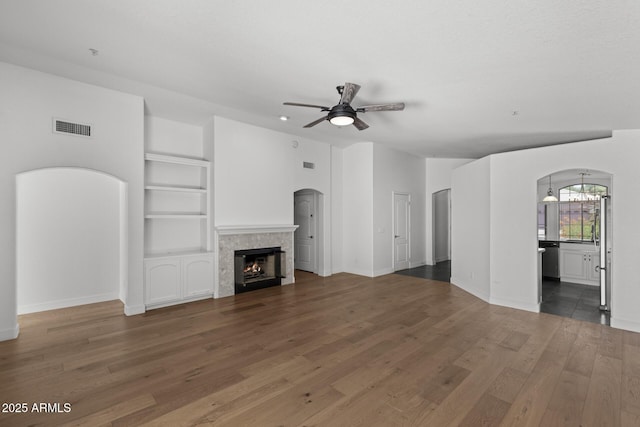 9631 E Palm Ridge Dr, Scottsdale, AZ 85260 - unfurnished living room featuring arched walkways, ceiling fan, wood finished floors, a fireplace, and built in features