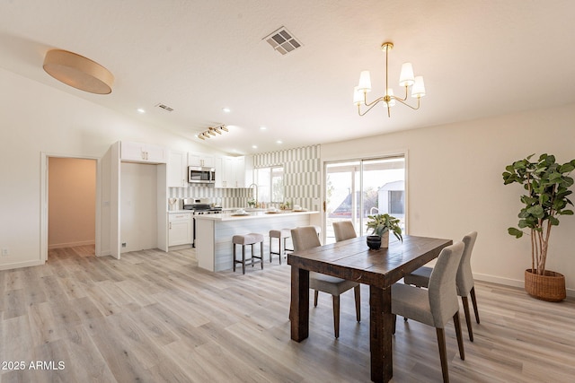 dining room with light wood-type flooring, lofted ceiling, a notable chandelier, and sink