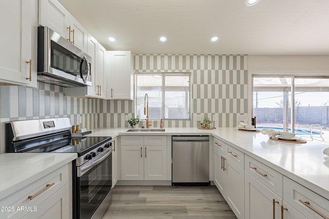 kitchen with backsplash, sink, white cabinetry, light hardwood / wood-style flooring, and stainless steel appliances