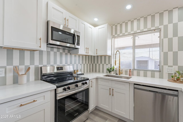 kitchen with white cabinetry, light hardwood / wood-style floors, appliances with stainless steel finishes, tasteful backsplash, and sink