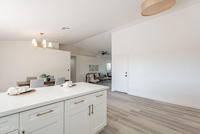 kitchen featuring ceiling fan with notable chandelier, white cabinets, vaulted ceiling, hanging light fixtures, and light wood-type flooring