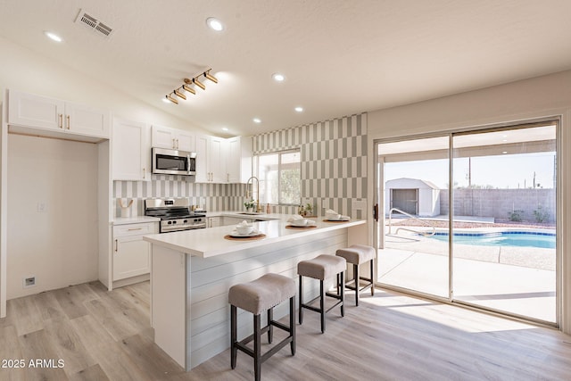 kitchen featuring a kitchen breakfast bar, white cabinetry, appliances with stainless steel finishes, and vaulted ceiling