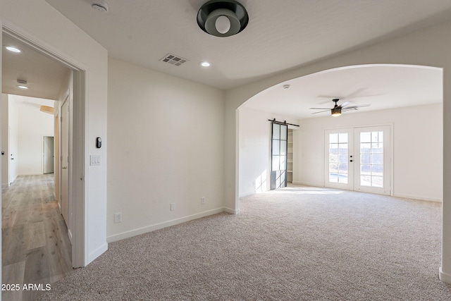 carpeted spare room with ceiling fan, a barn door, and french doors