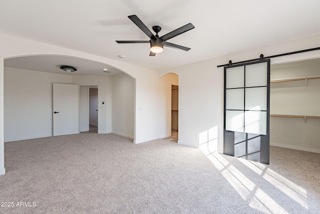 unfurnished bedroom with ceiling fan, a barn door, light colored carpet, a walk in closet, and a closet