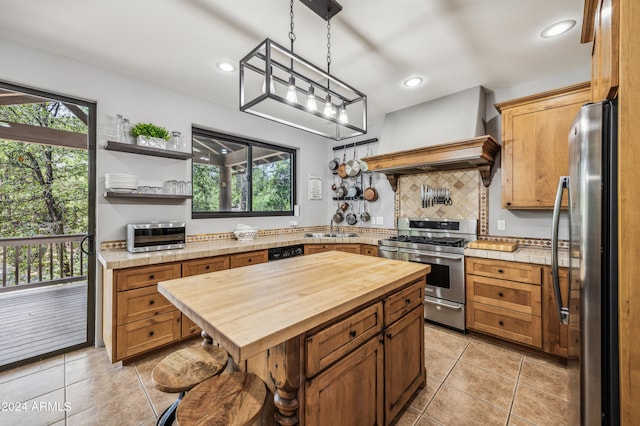 kitchen featuring premium range hood, stainless steel appliances, pendant lighting, wood counters, and light tile patterned floors