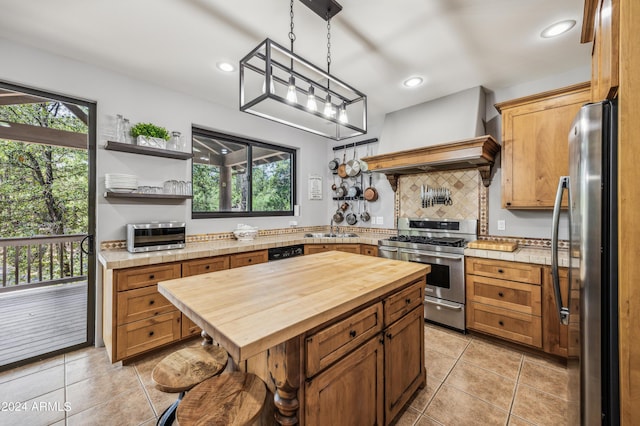 kitchen with premium range hood, a sink, a healthy amount of sunlight, wooden counters, and appliances with stainless steel finishes