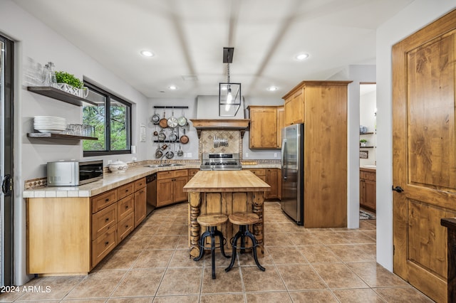 kitchen with light tile patterned floors, butcher block counters, a kitchen island, appliances with stainless steel finishes, and decorative light fixtures