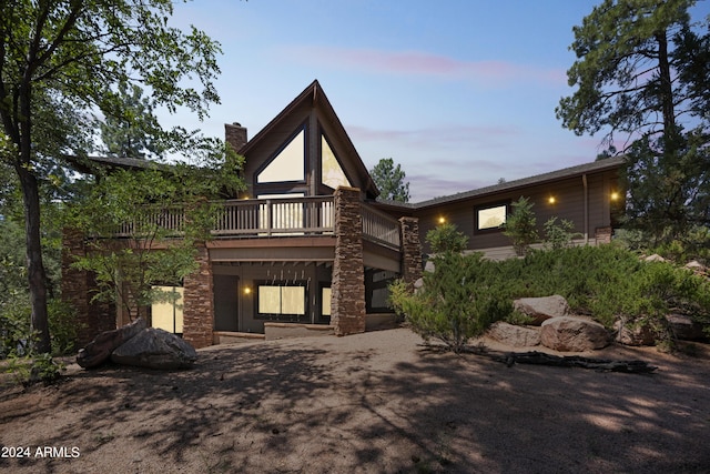 view of front facade with stone siding, a chimney, and a wooden deck