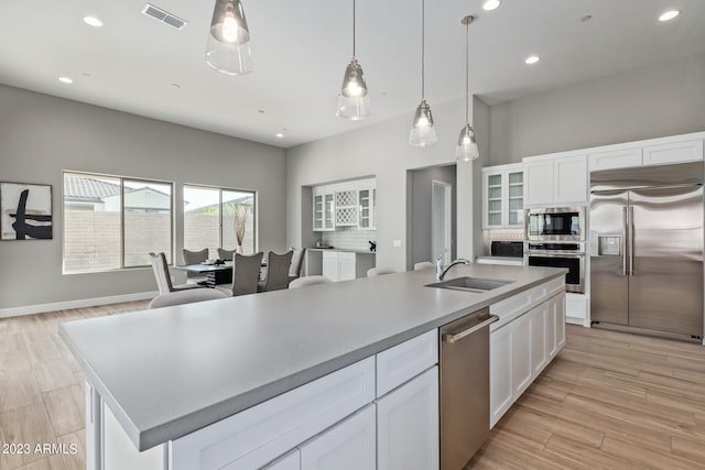 kitchen featuring white cabinetry, built in appliances, light hardwood / wood-style flooring, and an island with sink