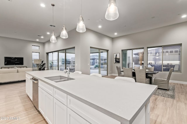 kitchen featuring a center island with sink, light hardwood / wood-style flooring, hanging light fixtures, sink, and white cabinets