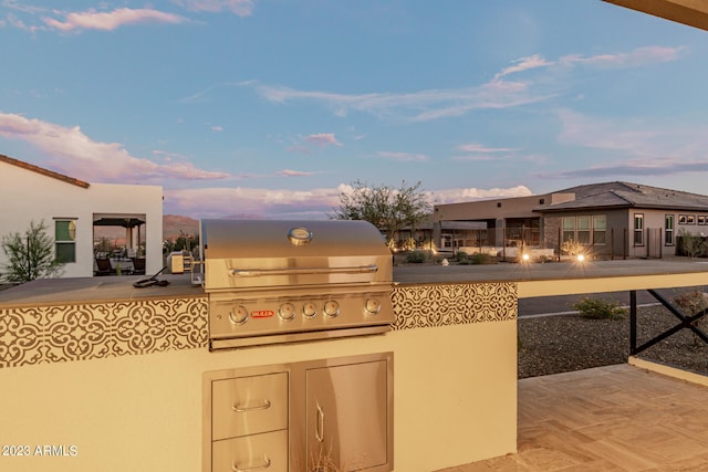 patio terrace at dusk featuring a grill and exterior kitchen