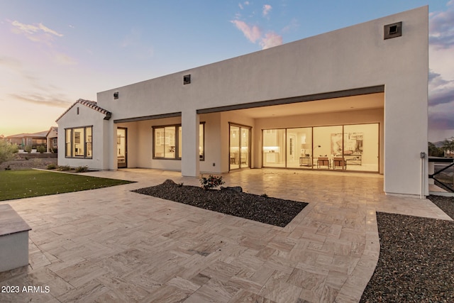 back house at dusk featuring a patio