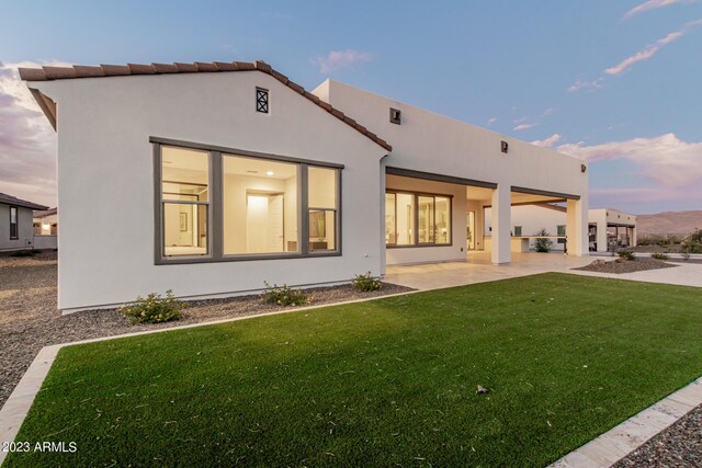 back house at dusk with a lawn and a patio