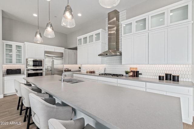 kitchen featuring pendant lighting, built in appliances, wall chimney exhaust hood, white cabinets, and light hardwood / wood-style floors