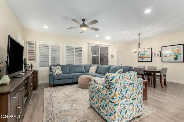 living room featuring ceiling fan with notable chandelier and light wood-type flooring