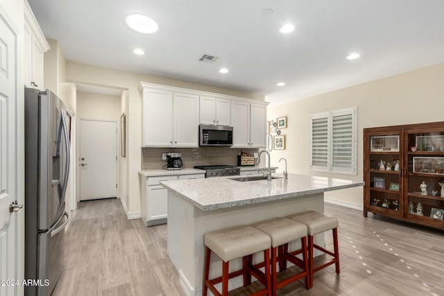 kitchen with sink, white cabinetry, stainless steel appliances, light stone countertops, and a kitchen island with sink