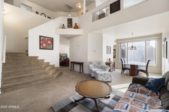 living room with carpet floors, visible vents, a high ceiling, a chandelier, and stairs