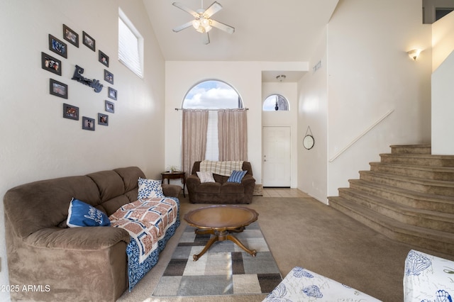 living area with visible vents, ceiling fan, stairway, carpet flooring, and high vaulted ceiling