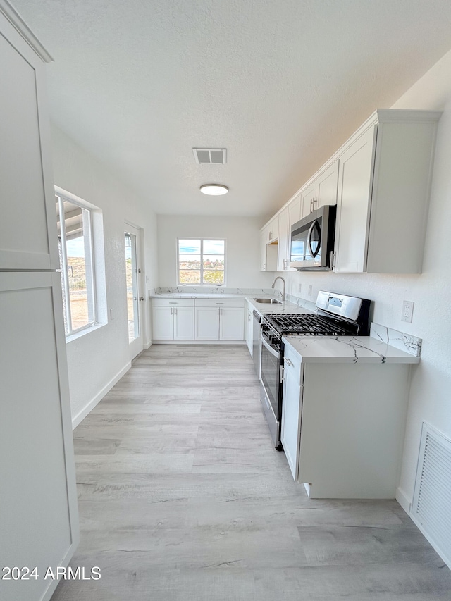 kitchen with light wood-type flooring, light stone counters, stainless steel appliances, sink, and white cabinets