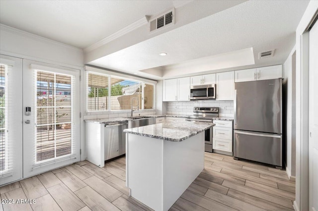 kitchen with appliances with stainless steel finishes, a kitchen island, white cabinetry, light stone counters, and light hardwood / wood-style flooring