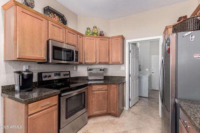 kitchen featuring appliances with stainless steel finishes, dark stone countertops, and washer / dryer