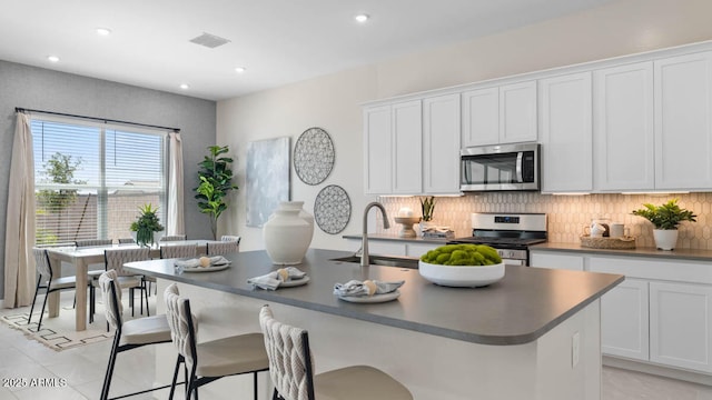 kitchen with stainless steel appliances, visible vents, decorative backsplash, a kitchen island with sink, and a sink