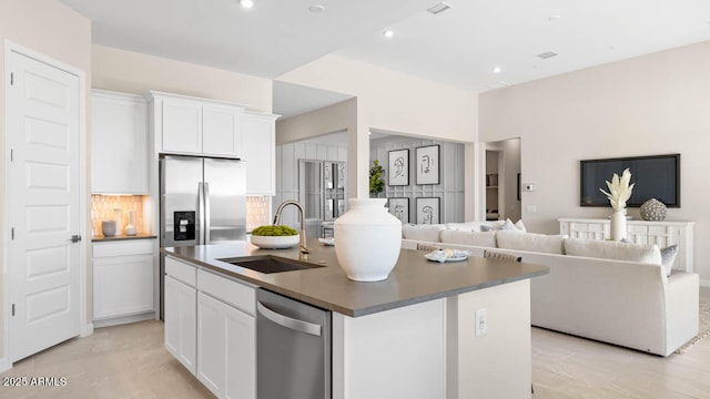 kitchen featuring stainless steel appliances, a sink, white cabinets, open floor plan, and decorative backsplash