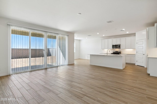 kitchen featuring an island with sink, open floor plan, stainless steel appliances, light countertops, and light wood-type flooring