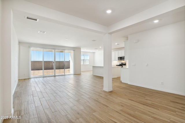 unfurnished living room with visible vents, light wood-style flooring, and baseboards