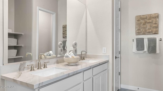 full bathroom featuring double vanity, baseboards, and a sink