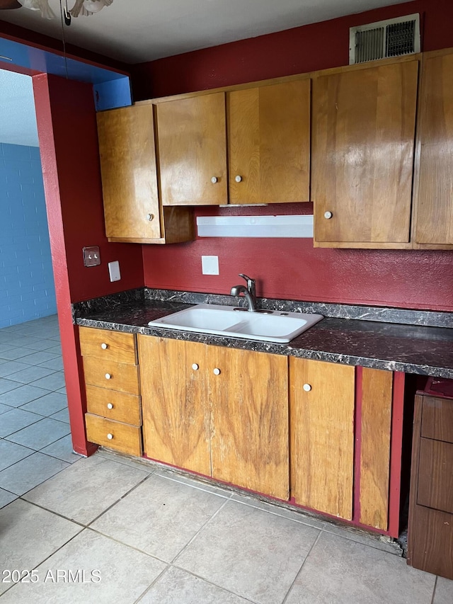 kitchen featuring light tile patterned floors, visible vents, dark countertops, brown cabinets, and a sink