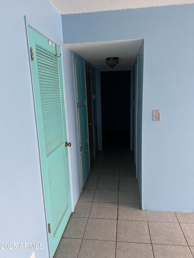 hall with a textured ceiling and light tile patterned flooring