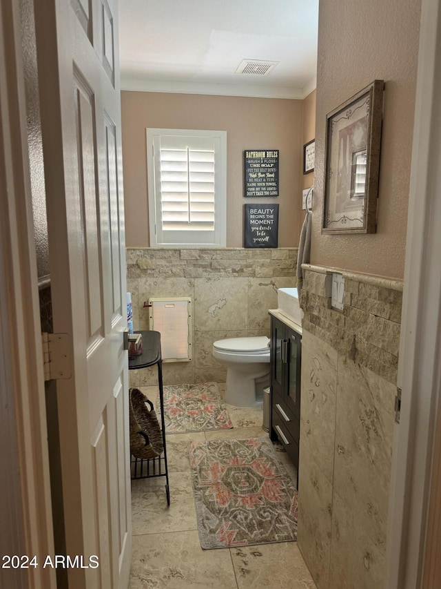 bathroom featuring tile patterned flooring, toilet, vanity, tile walls, and ornamental molding