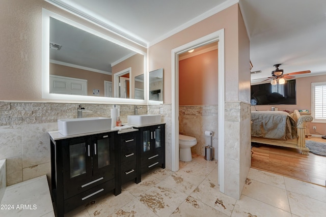 bathroom with ornamental molding, vanity, ceiling fan, tile walls, and toilet