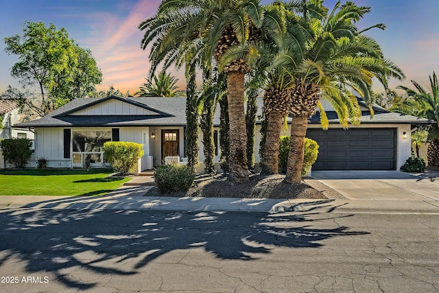 view of front of home featuring concrete driveway, roof with shingles, an attached garage, a front lawn, and board and batten siding