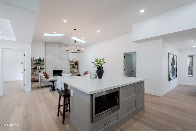 kitchen featuring a center island, stainless steel microwave, gray cabinetry, a high end fireplace, and vaulted ceiling with skylight