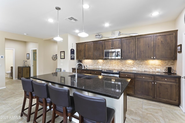 kitchen featuring visible vents, a breakfast bar, a sink, decorative backsplash, and stainless steel appliances