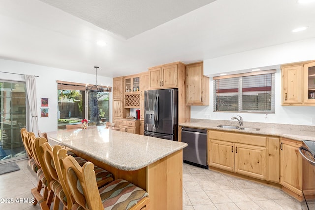 kitchen featuring a breakfast bar area, light brown cabinets, stainless steel appliances, a sink, and a center island