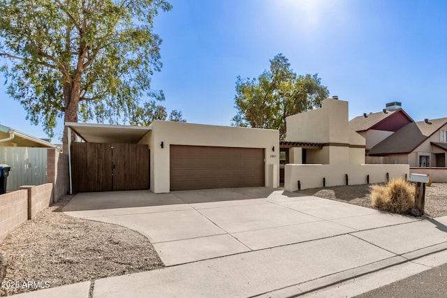 adobe home featuring a garage, concrete driveway, fence, a carport, and stucco siding