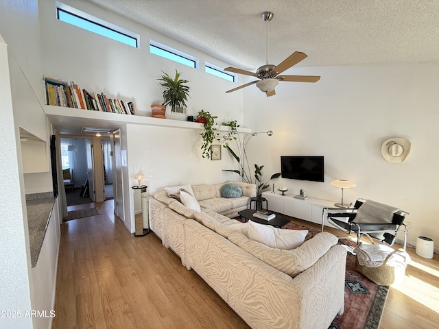 living room with a towering ceiling, a textured ceiling, ceiling fan, and light hardwood / wood-style floors