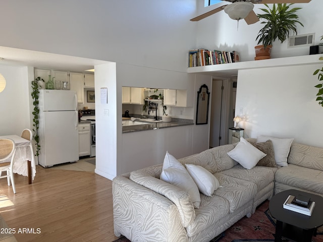 living room featuring a towering ceiling, ceiling fan, and light hardwood / wood-style flooring