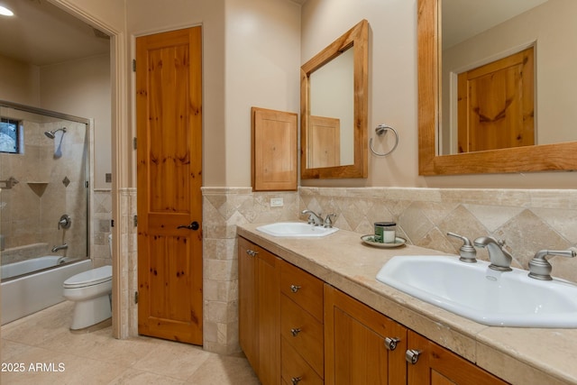 full bathroom with tile patterned flooring, enclosed tub / shower combo, toilet, vanity, and tile walls