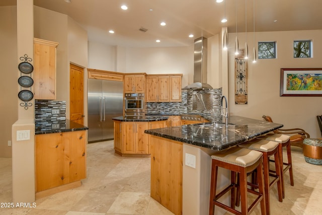 kitchen with pendant lighting, dark stone counters, wall chimney range hood, kitchen peninsula, and stainless steel appliances