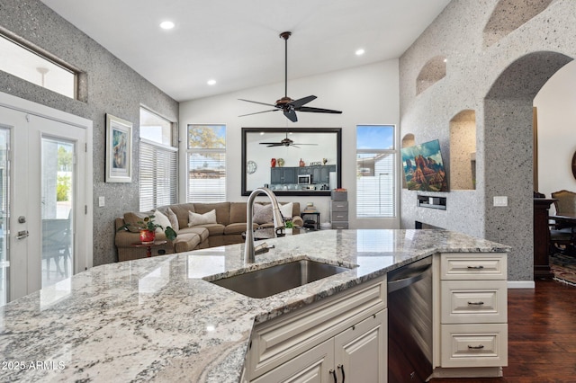 kitchen with light stone counters, stainless steel dishwasher, open floor plan, vaulted ceiling, and a sink