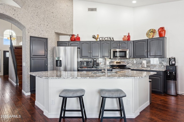 kitchen featuring arched walkways, dark wood-style floors, stainless steel appliances, a kitchen bar, and a sink