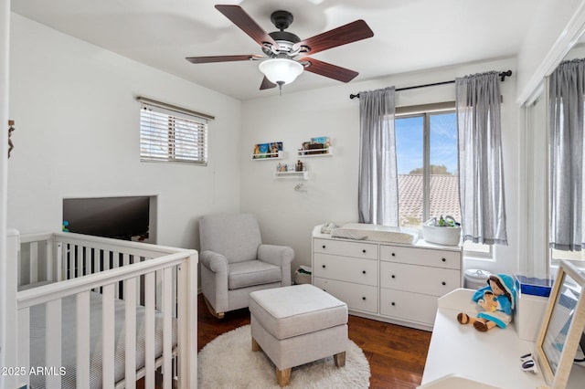 bedroom with dark wood-type flooring, a nursery area, and a ceiling fan