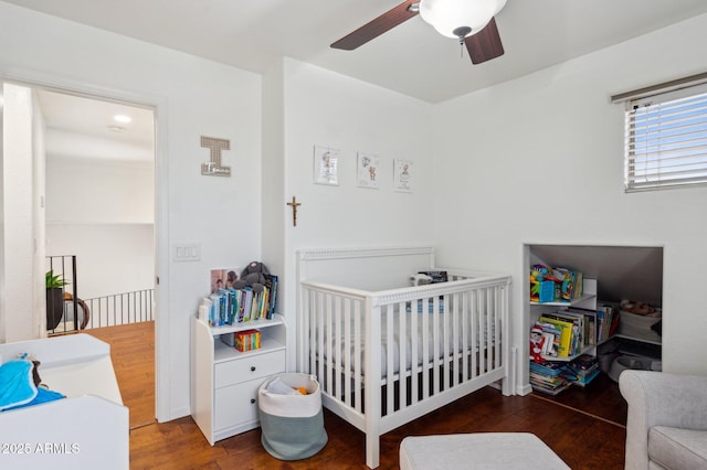 bedroom with a nursery area, ceiling fan, and wood finished floors